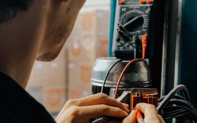 Electrician using a multimeter to check voltages in an industrial setting.